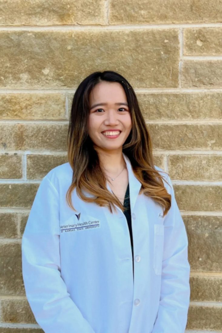 Smiling female veterinarian in white coat standing against a stone wall