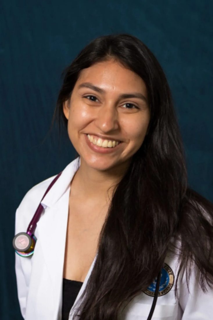 Smiling female veterinarian with stethoscope in white coat against dark blue background